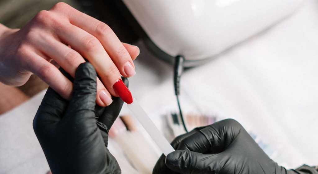 styliste ongulaire à domicile portant des gant noir. Limage sur un ongle synthétique vernis de rouge pour la main d'une cliente - choisir son vernis